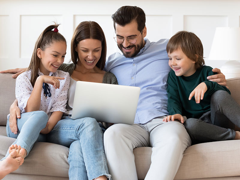 There's a family on a couch smiling as they have a video call with their relatives from another state.