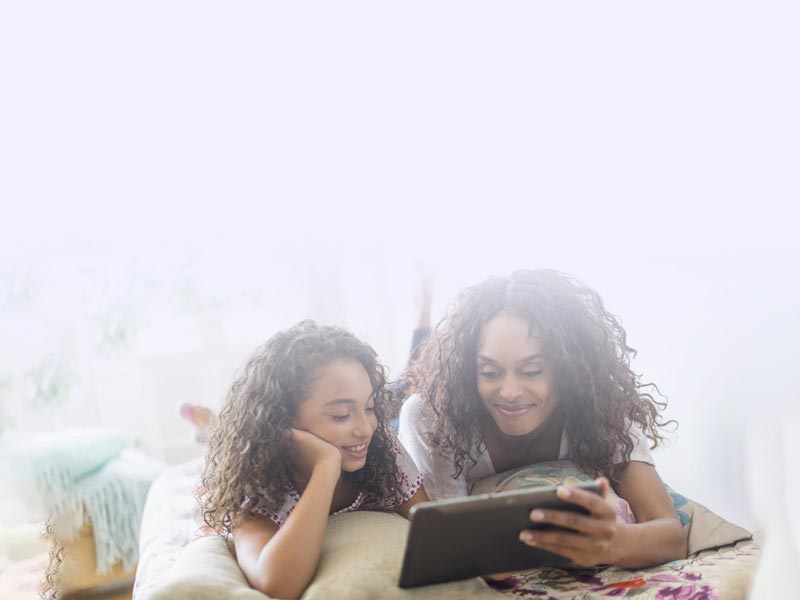 parent and child smiling while enjoying a movie on their tablet