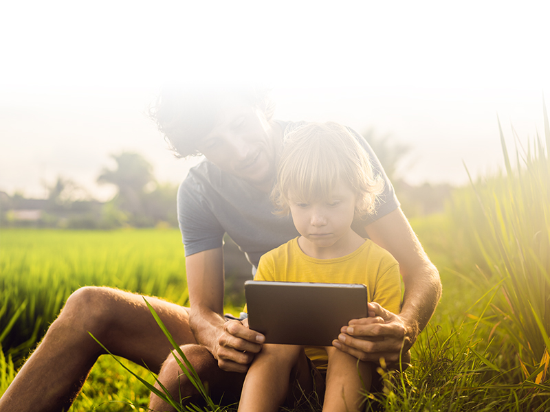 parent and child reading on a tablet in their backyard