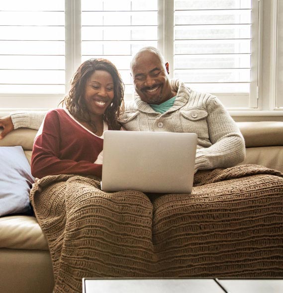 smiling couple on couch watching TV on laptop